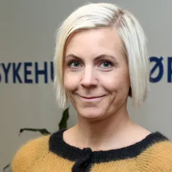 En smilende kvinne foran en vegg med Sykehusinnkjøps logo på.