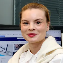 En smilende kvinne sitter foran en dataskjerm